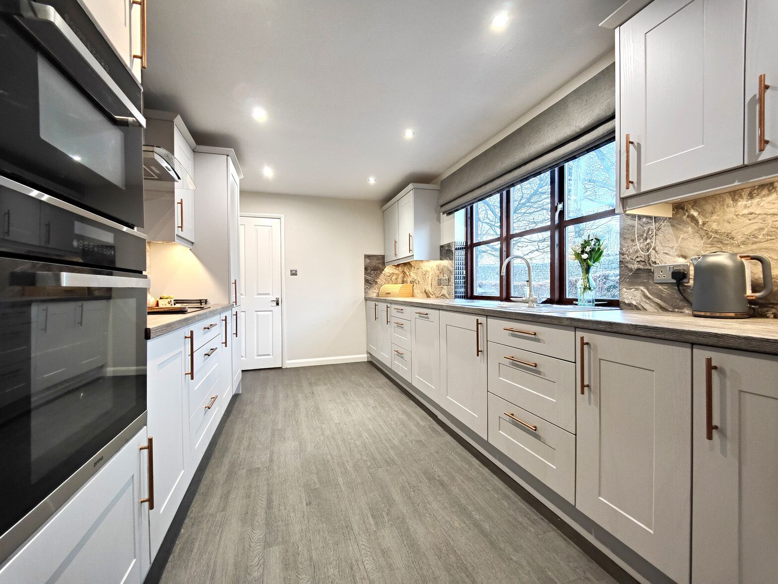 A modern kitchen with white cabinets, a large window, and a built-in oven.