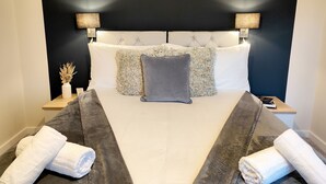 A neatly made bed with a dark headboard, white linens, and decorative pillows. There are two bedside tables with lamps and a small vase with dried flowers. - Yewtree House (Penrith)
