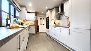 A modern kitchen with white cabinetry, a wooden countertop, and a view of the outdoors through large windows. - Yewtree House (Penrith)
