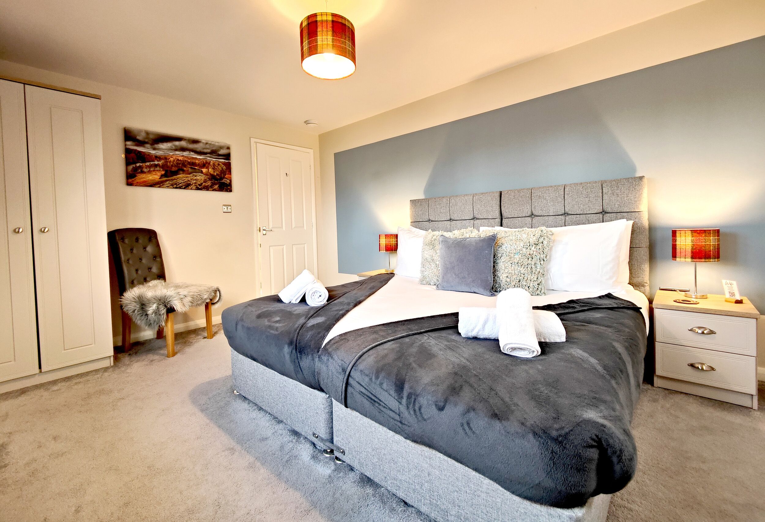 A bedroom with a large bed, a chair, a wardrobe, and a painting on the wall.
