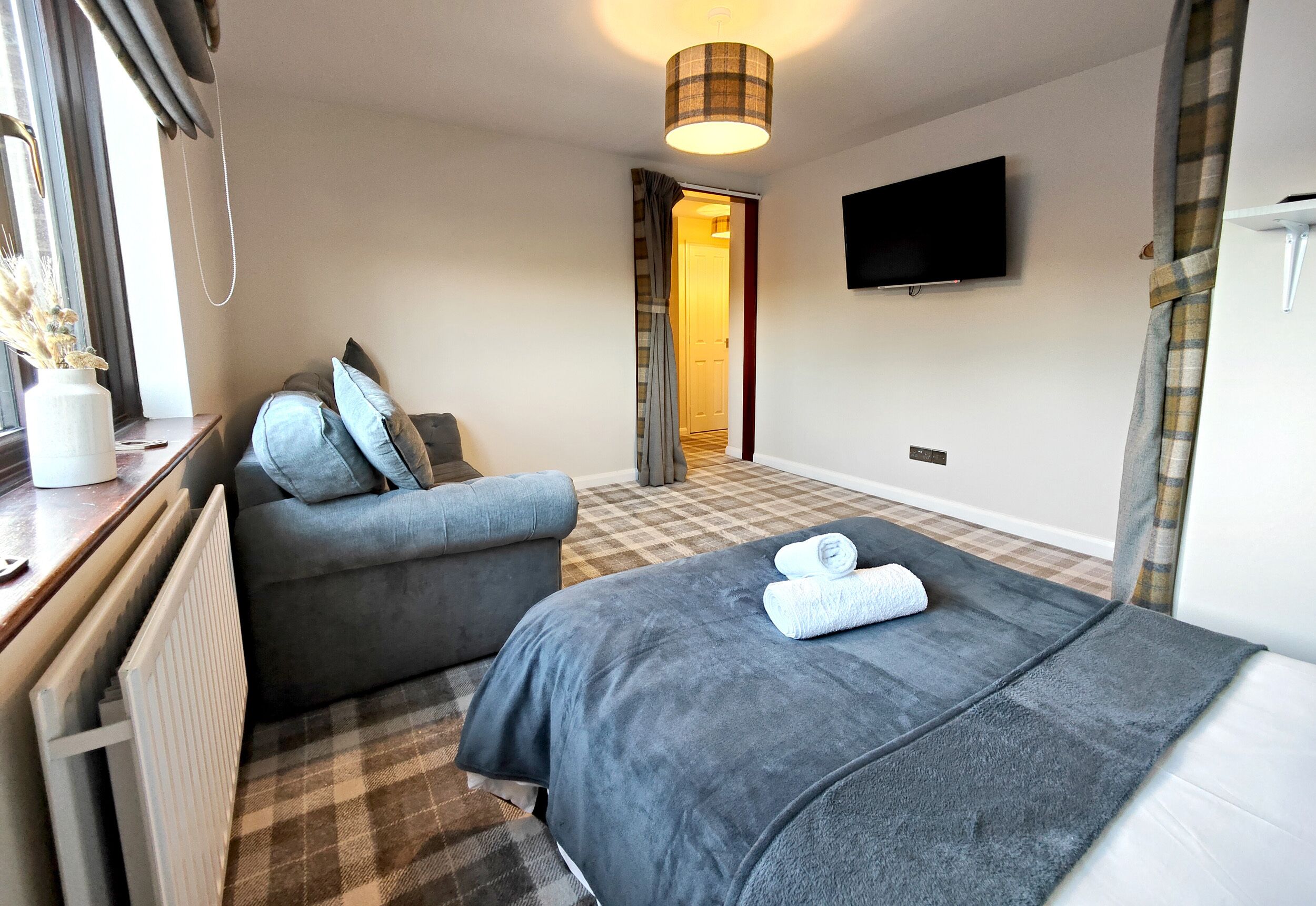 A hotel room with a bed, a sofa, a TV, and a window with curtains.