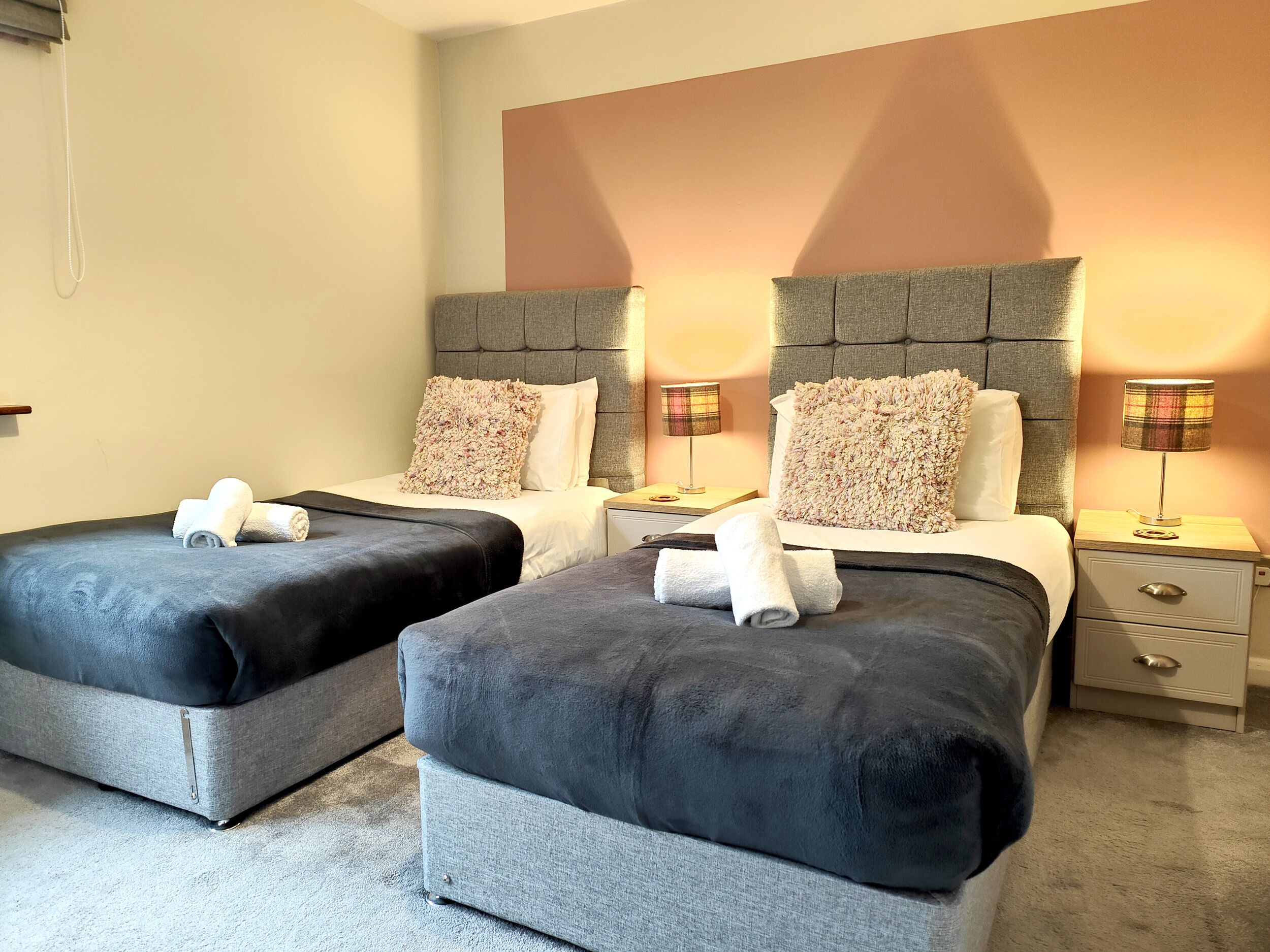 Une chambre d’hôtel avec deux lits, chacun doté d’une tête de lit grise, de draps blancs et d’un oreiller moelleux. Il y a deux tables de chevet avec des lampes et un petit tiroir.
