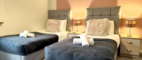 Une chambre d’hôtel avec deux lits, chacun doté d’une tête de lit grise, de draps blancs et d’un oreiller moelleux. Il y a deux tables de chevet avec des lampes et un petit tiroir.