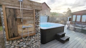 A hot tub with a wooden deck and stone wall, a wooden door, and a metal showerhead. - Yewtree House (Penrith)