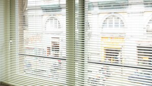 A window with horizontal blinds, through which a building with arched windows and a yellow awning is visible. - CIVICO 237 (Naples)