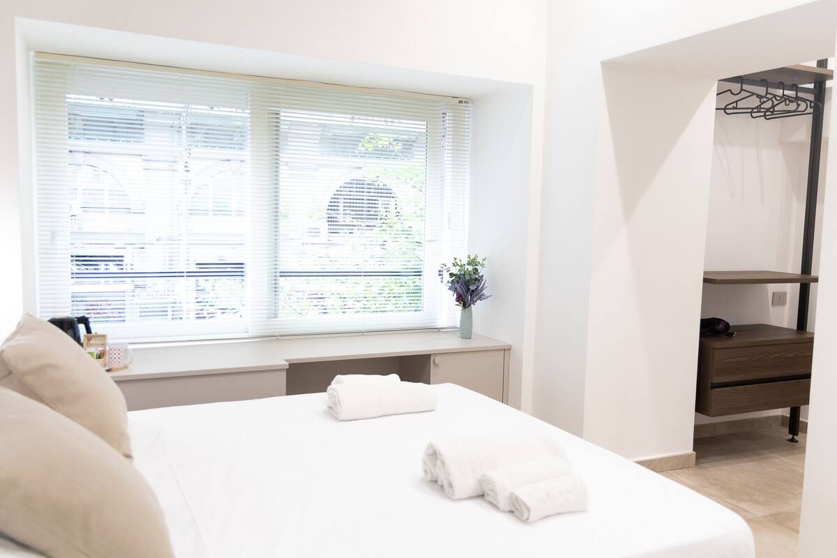 Un dormitorio con cama, escritorio y ventana con persianas.