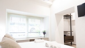 A hotel room with a bed, a window with blinds, a bedside table with a vase, and a wardrobe with a mirror. - CIVICO 237 (Naples)