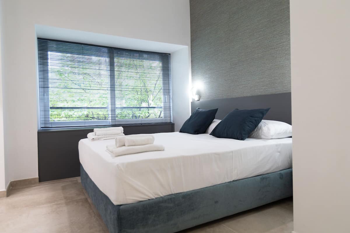 Un dormitorio moderno con cama, almohadas y una ventana con persianas.