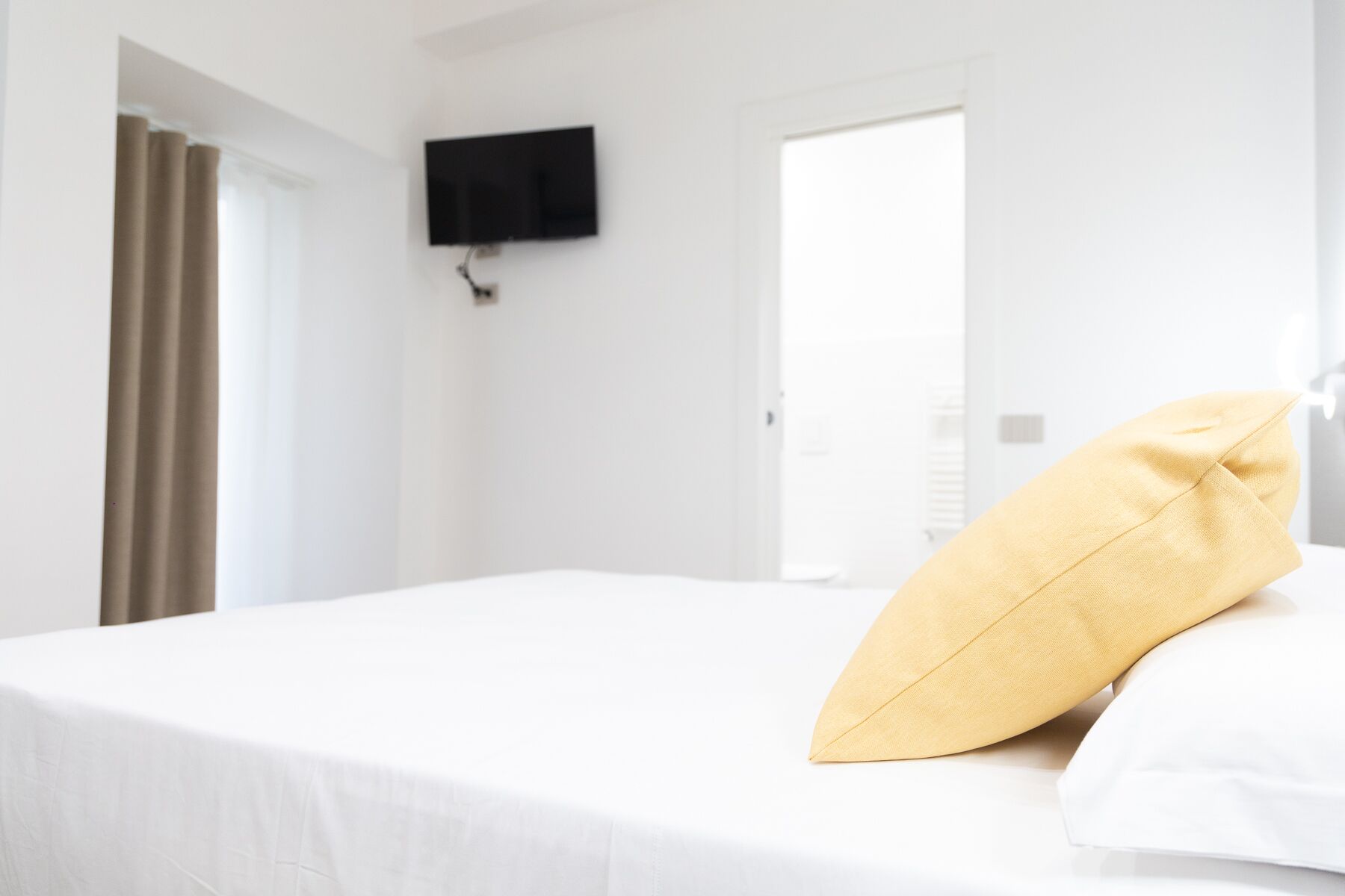 A hotel room with a bed, a television mounted on the wall, and a door leading to another room.