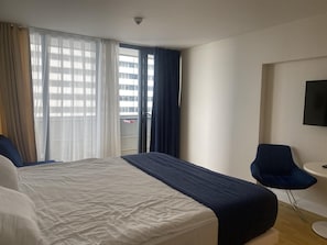 A hotel room with a bed, a chair, a small table, and a TV on the wall. - Orbi City Apartament (Batumi)