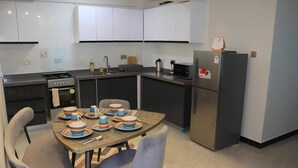 Une cuisine moderne avec des meubles blancs, des appareils en acier inoxydable et une table à manger pour quatre personnes.
