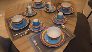 Une table de salle à manger ronde, dressée pour huit personnes, avec une vaisselle assortie : assiettes, bols et tasses.