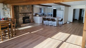 A spacious kitchen with a stone fireplace, wooden ceiling beams, and a central island with bar stools. - West World (Beaver Dam)
