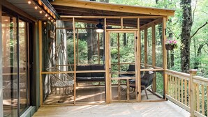 Une terrasse en bois avec une structure vitrée, un espace salon et des jardinières suspendues.