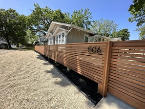 Una recinzione di legno con il numero 506, un vialetto sterrato e una casa con tetto spiovente sullo sfondo.
