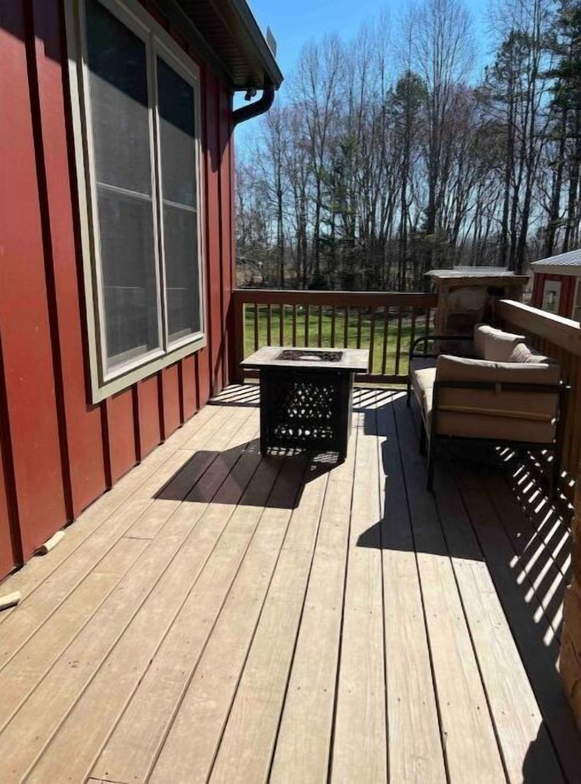 A wooden deck with a red building, a black trash bin, and a beige outdoor seating area.