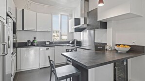 A modern kitchen with white cabinets, a central island, and a view of the city. - Grand 5 Pièces Haussmannien (Paris)