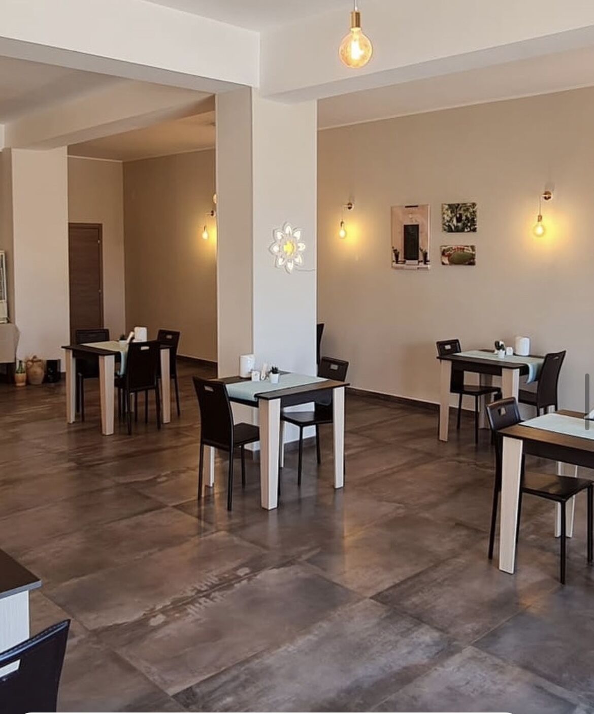 A spacious dining area with multiple tables and chairs, a decorative wall piece, and a modern light fixture.