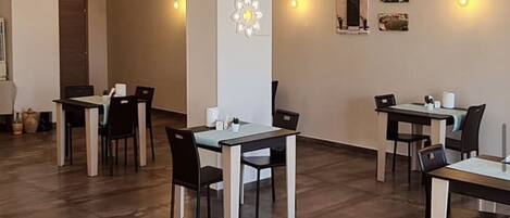 A spacious dining area with multiple tables and chairs, a decorative wall piece, and a modern light fixture.