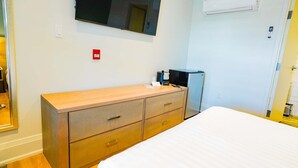 Ein Hotelzimmer mit einem Holzkasten, einem Bett, einem flachbildfernseher an der Wand und einer Klimaanlage.