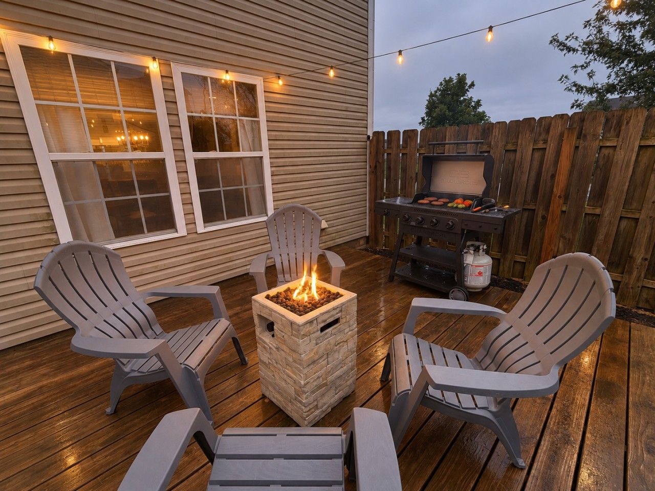 Un patio exterior con sillas Adirondack, un hogar para fogata cuadrado y una parrilla.