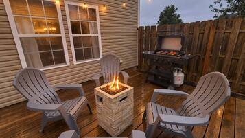 Un patio exterior con sillas Adirondack, un hogar para fogata cuadrado y una parrilla.