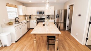 A modern kitchen with white cabinetry, a wooden island, stainless steel appliances, and a hanging pendant light. - Acoustic Oasis- RUOFF Music & POOL TABLE sleeps 10 (Noblesville)
