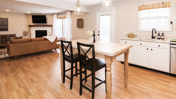 A modern kitchen with white cabinets, a wooden dining table, and two black chairs. - Acoustic Oasis- RUOFF Music & POOL TABLE sleeps 10 (Noblesville)