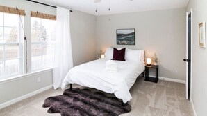 A bedroom with a bed, a nightstand, a lamp, a painting on the wall, and a large window with curtains. - Acoustic Oasis- RUOFF Music & POOL TABLE sleeps 10 (Noblesville)