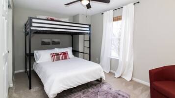 Una cama litera con ventilador de techo, una silla roja y una ventana con cortinas.