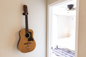 A guitar hanging on a wall in a room with a door leading to another space.
