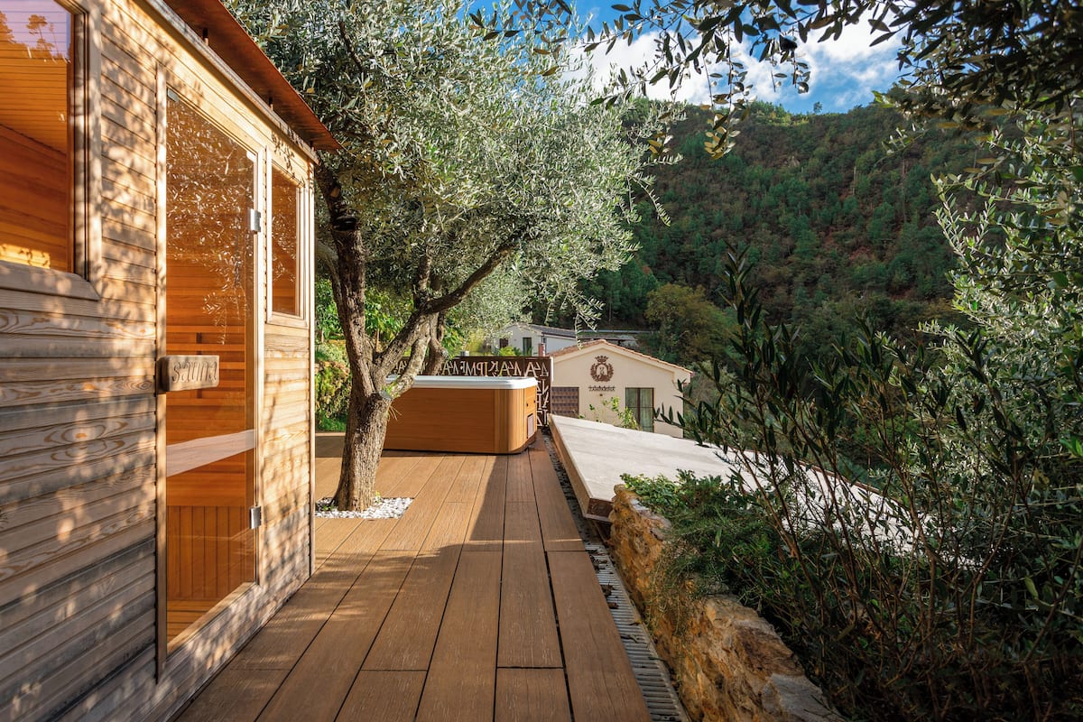 A wooden cabin with a sauna, a hot tub, and a deck overlooking a forested hillside.