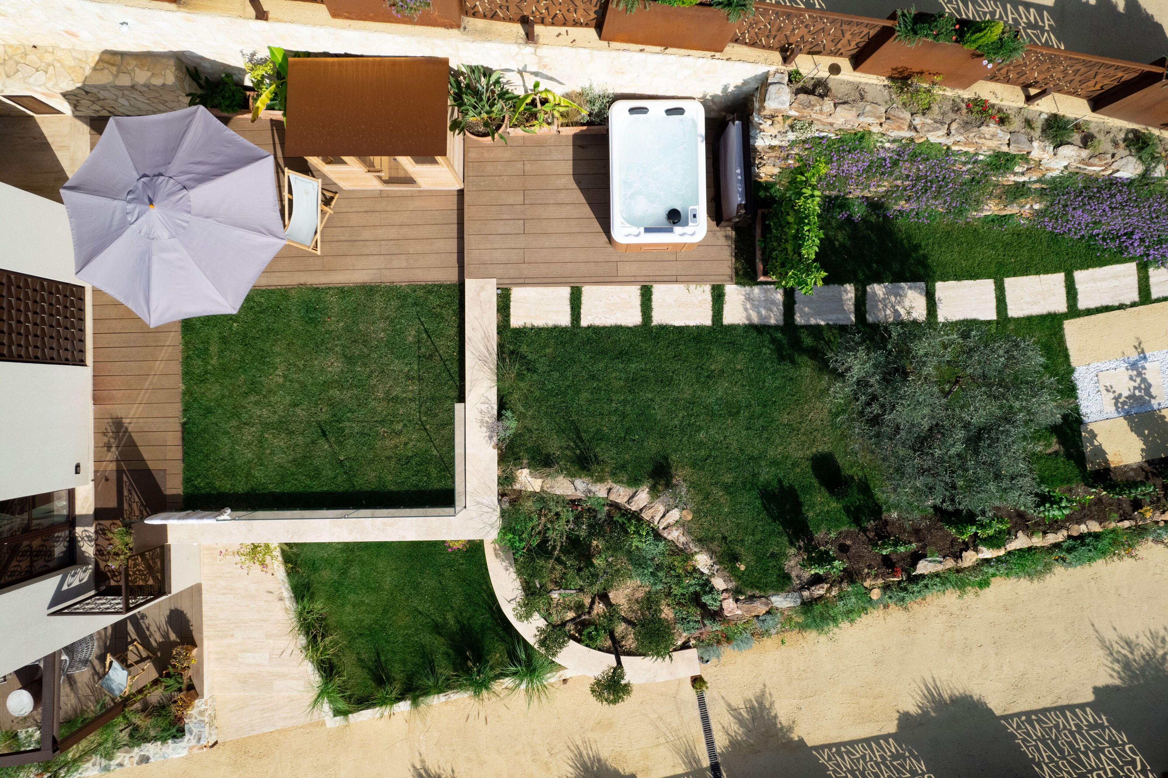 An aerial view of a landscaped outdoor area with a hot tub, a wooden deck, and a grassy lawn.
