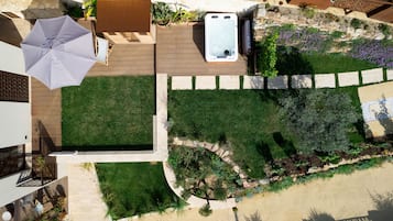 An aerial view of a landscaped outdoor area with a hot tub, a wooden deck, and a grassy lawn.