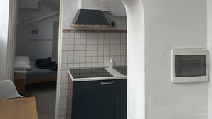 Una cocina compacta con salpicadero de azulejos, un fogón y un lavamanos pequeño. Un cartel con texto motivacional está colgado en la pared.
