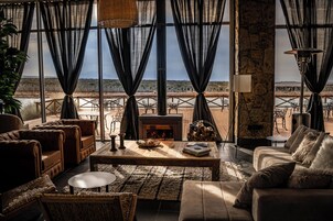 Una sala de estar acogedora con chimenea, asientos cómodos y vistas al paisaje desértico a través de amplios ventanales.