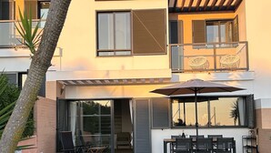 Ein modernes, zweistöckiges Haus mit einer Terrassenanlage, die Gartenmöbel und einen großen Sonnenschirm beinhaltet.
