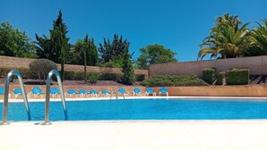 Ein Swimmingpool mit blauem Wasser, umgeben von einer niedrigen Mauer und mehreren blauen Liegestühlen.