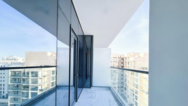 A modern apartment with a balcony, large windows, and a view of other buildings. - Spacious Studio With Balcony in AL Majan (Dubai)