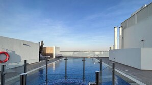 A rooftop swimming pool with clear blue water, surrounded by white walls and a glass barrier. - Spacious Studio With Balcony in AL Majan (Dubai)
