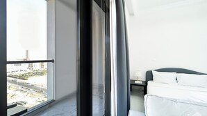 A modern hotel room with a balcony, a bed, a nightstand, and a view of the cityscape. - Spacious Studio With Balcony in AL Majan (Dubai)