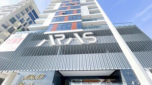 A modern building with a prominent 'ARAS' sign. It features a vertical facade with alternating red and blue stripes, and a sign indicating 'For Rent'. - Spacious Studio With Balcony in AL Majan (Dubai)