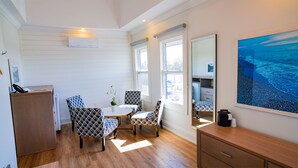Habitación compacta con un escritorio de madera, dos sillas estampadas, una mesita pequeña y un ventanal con vistas a la playa.