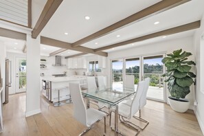 A modern kitchen with white cabinetry, a glass dining table, and a large potted plant.