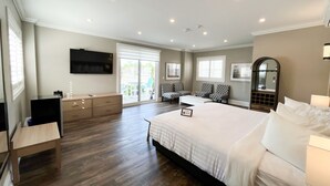 A bedroom with a large bed, a desk, a chair, a TV, and a sliding glass door to a balcony.