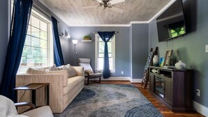 Un salon comprenant un canapé, un fauteuil, une table basse, un téléviseur fixé au mur et un ventilateur de plafond.