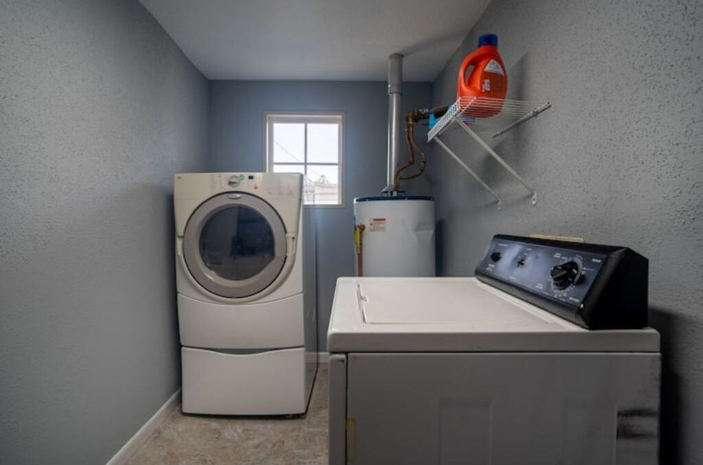 A laundry room with a front-loading washer and dryer, a water heater, and a window.
