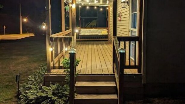 Une terrasse en bois avec un escalier menant à un porche abrité, le tout entouré d’un mur extérieur de couleur sombre.