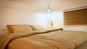 Ein Schlafzimmer mit einem Bett, einem Nachttisch mit Blumenvase und einem Fenster mit Jalousien.