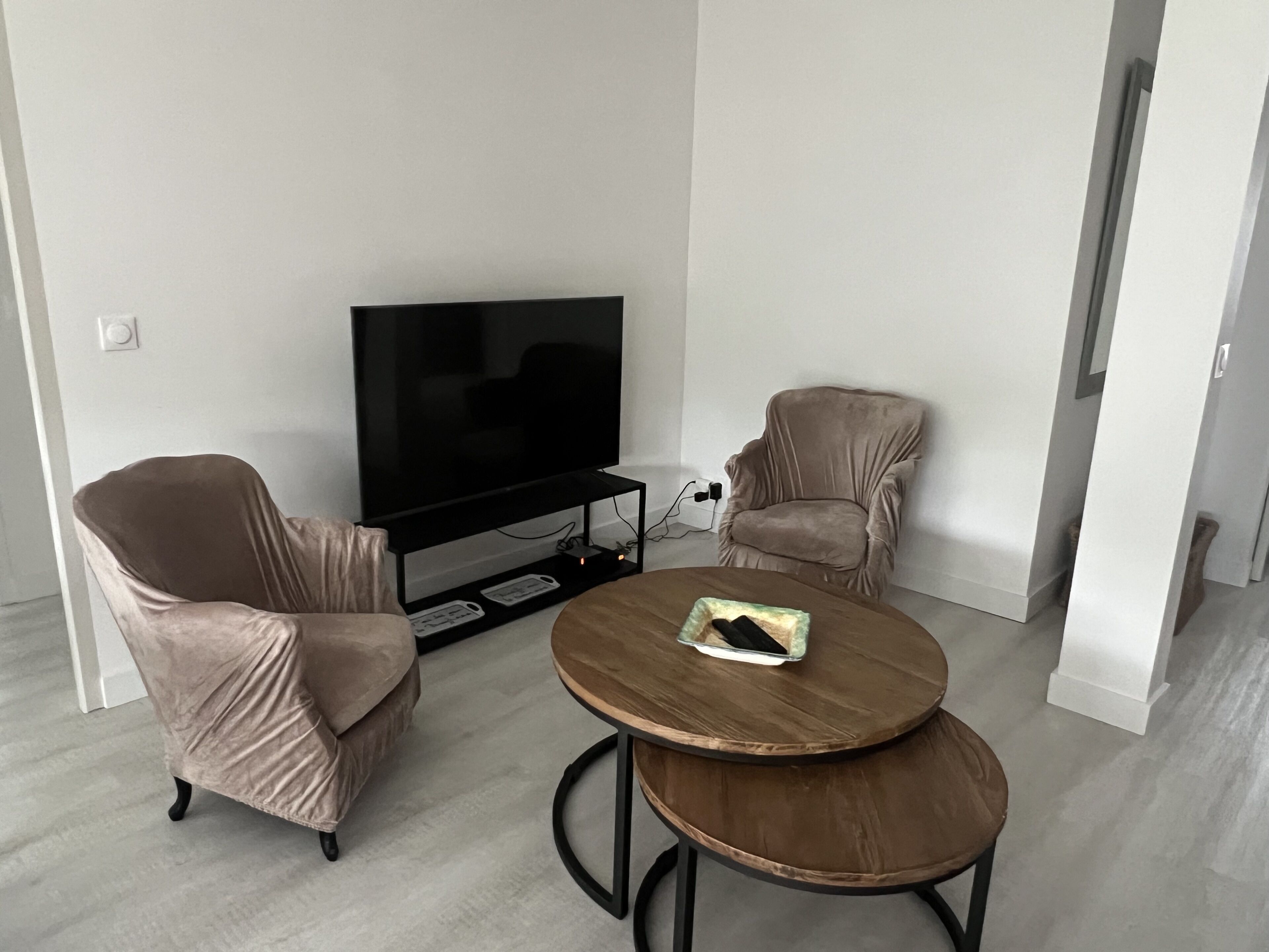 A modern living room with a flat-screen TV, two cushioned armchairs, and a small wooden coffee table.